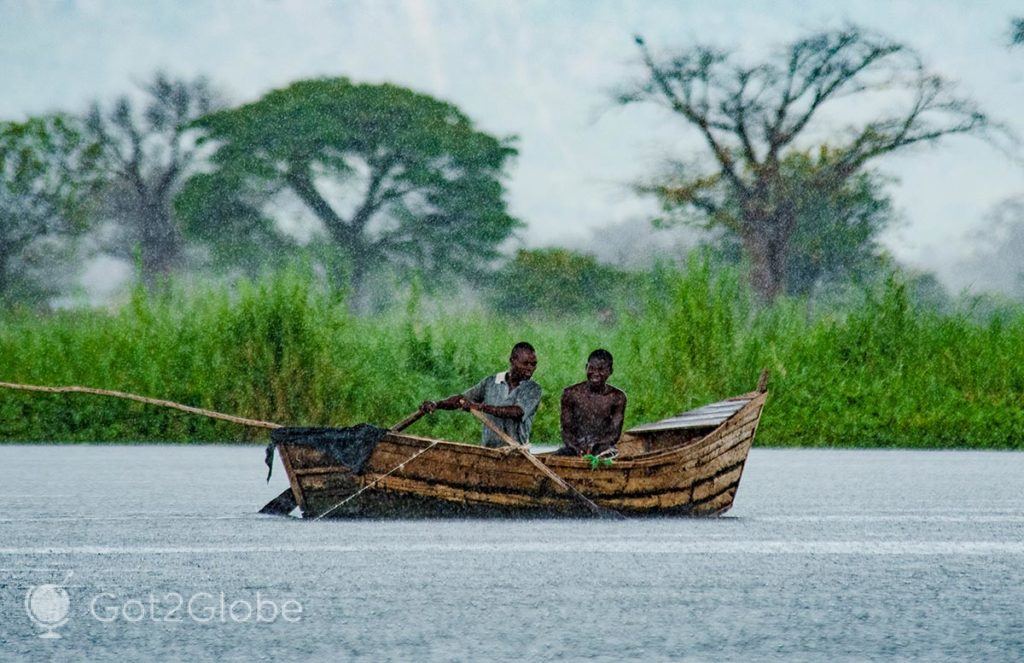 Pescadores num barco, sob uma densa chuvada tropical.