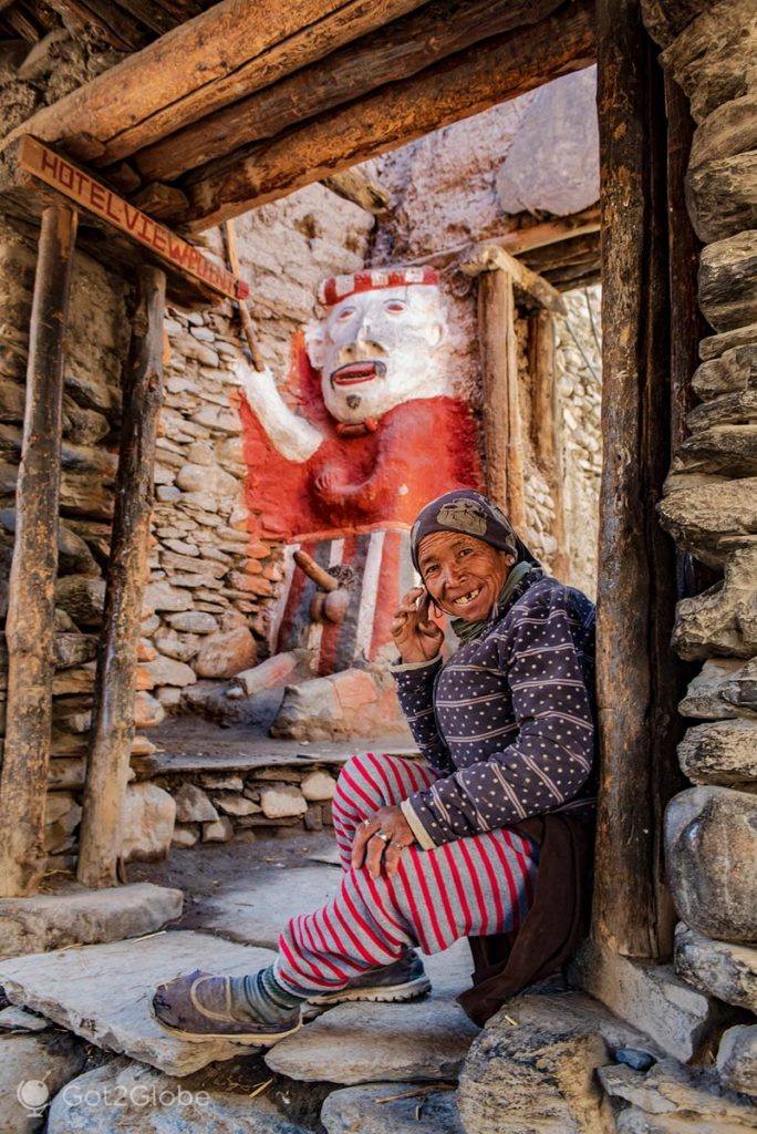 Mulher de Kagbeni conversa ao telefone com um totem da masculinidade em fundo